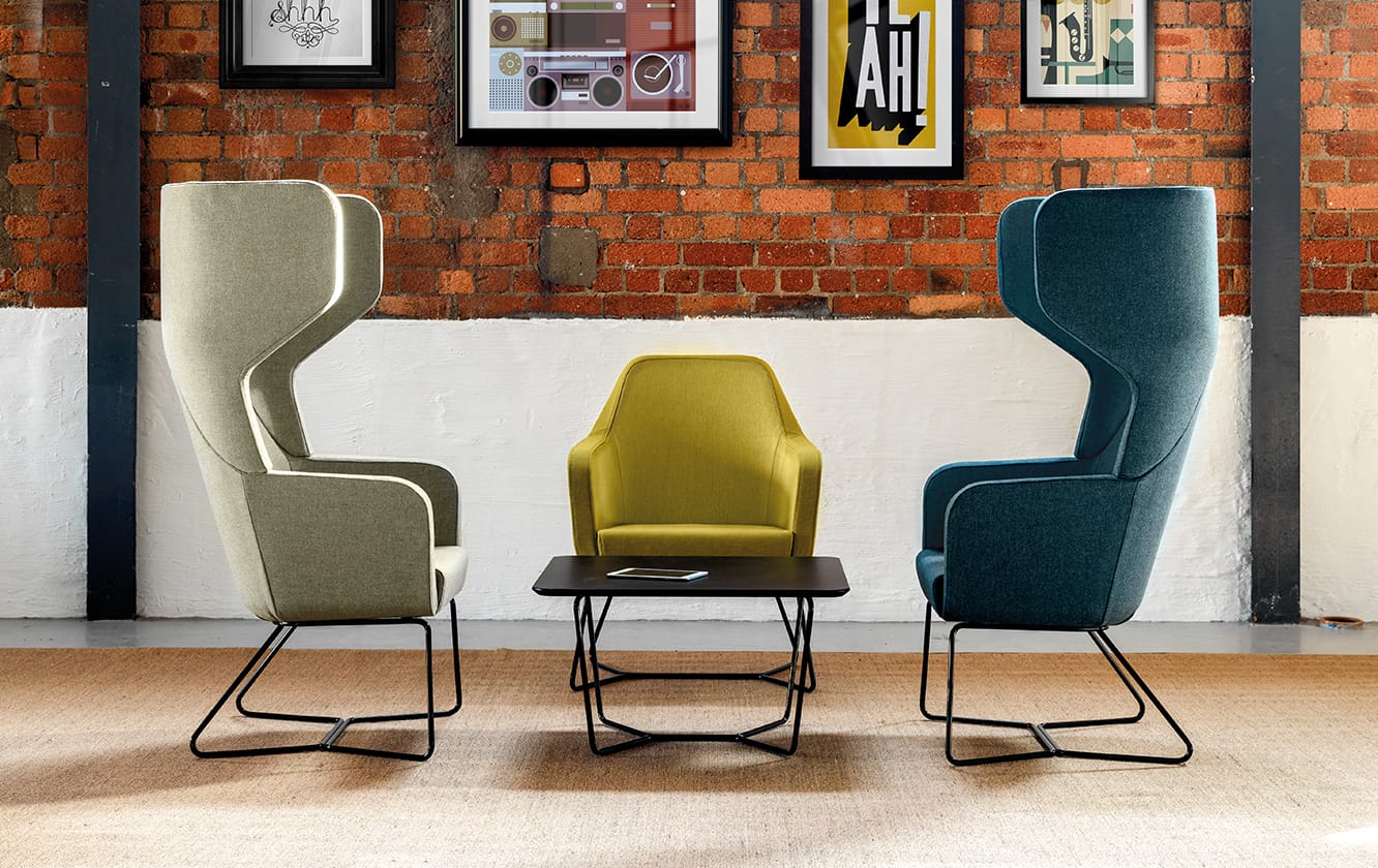 Three colourful lounge chairs for offices in a room with a brick wall.
